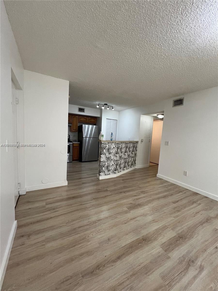 A living area with wood-look flooring leads to a kitchen featuring a floral-patterned breakfast bar — 3700 N 56th Ave # 1012, Hollywood FL 33021, HOLLYWOOD, FL