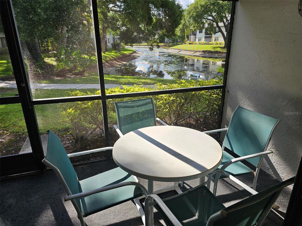 A screened-in patio features a round table and four chairs overlooking a pond — 4655 W 46TH STREET COURT UNIT 103, BRADENTON, FL