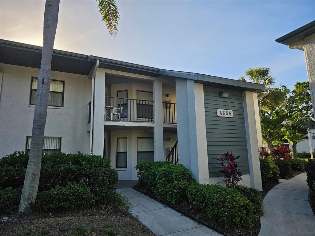 A two-story apartment building exterior features a balcony, a walkway, and landscaped shrubbery — 4655 W 46TH STREET COURT UNIT 103, BRADENTON, FL