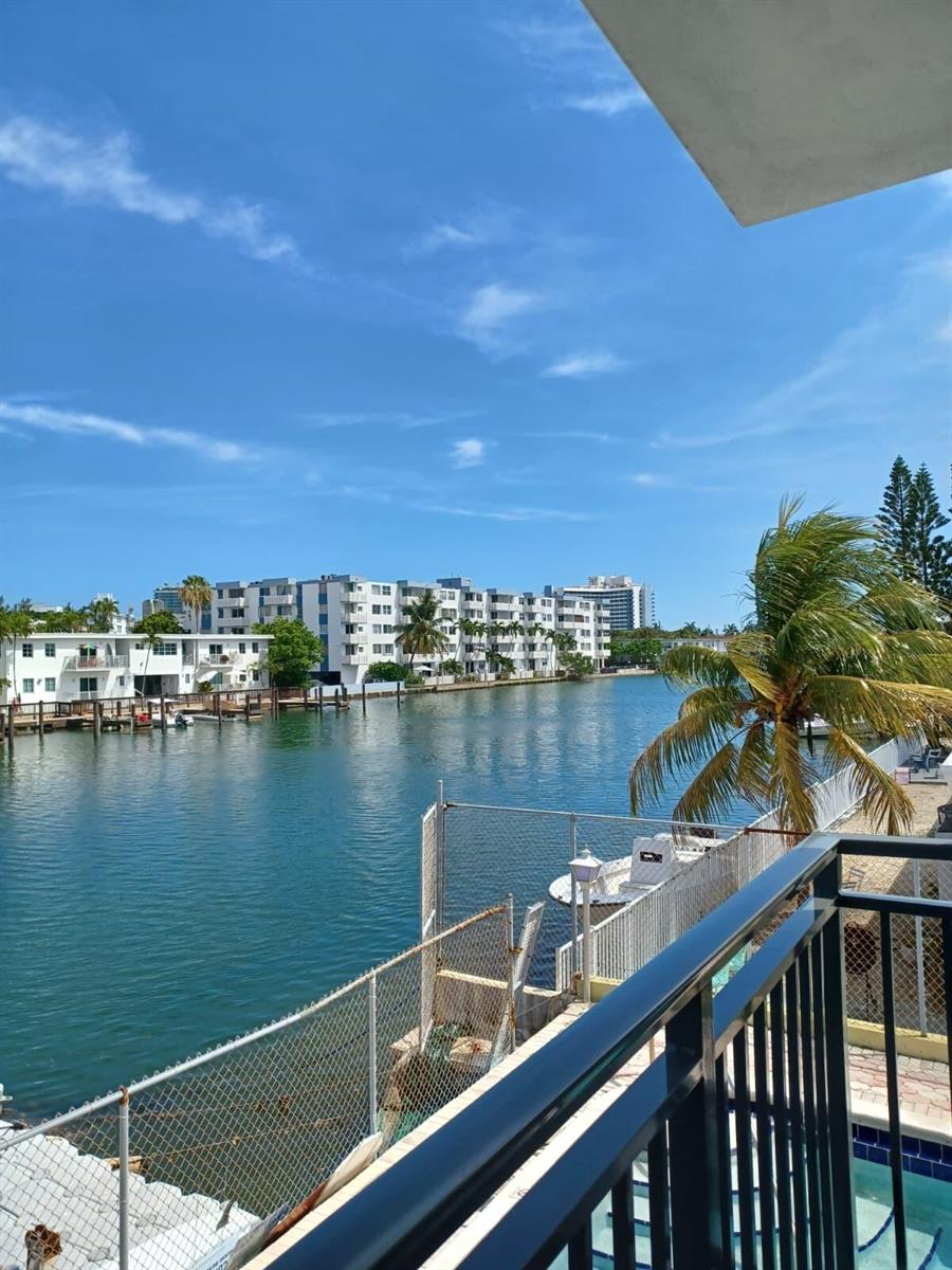 A view from a balcony overlooking a canal with waterfront buildings and palm trees — 8001 N Crespi Boulevard # 2c, Miami Beach FL 33141, MIAMI BEACH, FL