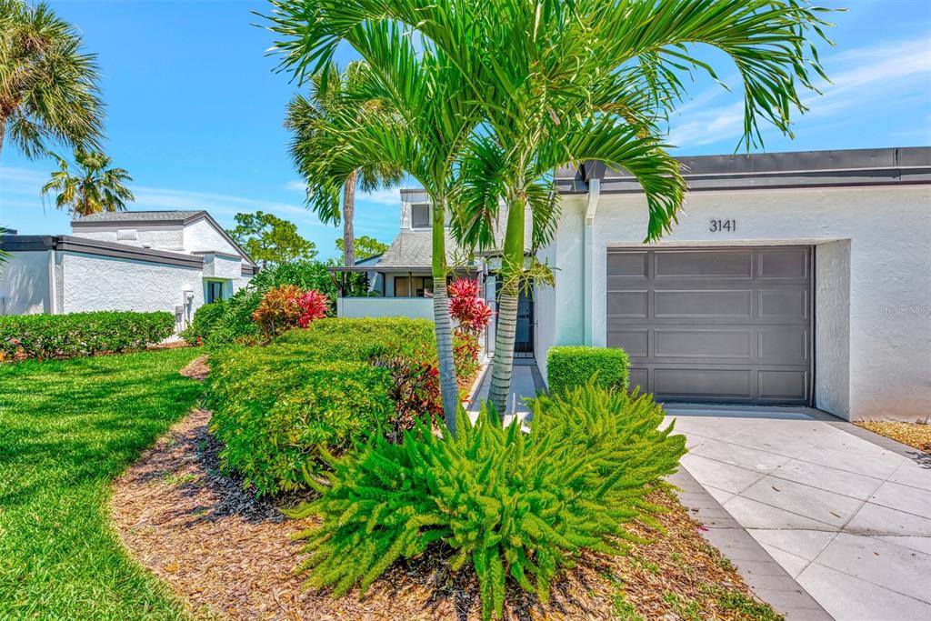 A white house exterior features a gray garage door, palm trees, and landscaped front yard — 3141 HEATHERWOOD LANE, SARASOTA, FL