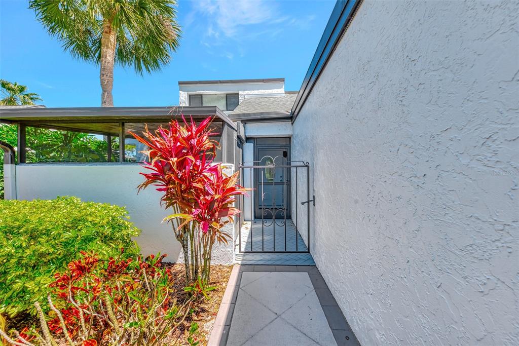A paved walkway leads to a gated entryway beside a white stucco wall and landscaping — 3141 HEATHERWOOD LANE, SARASOTA, FL