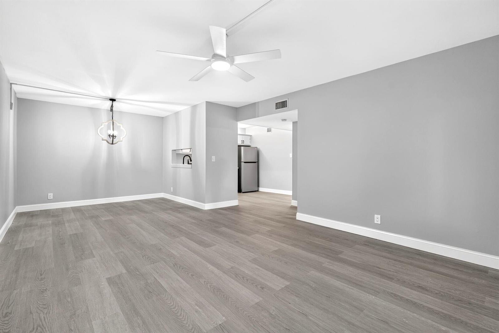 An empty room with gray walls, wood-look flooring, a ceiling fan, and a dining chandelier — 6495 Chasewood Drive # B, Jupiter FL 33458, JUPITER, FL