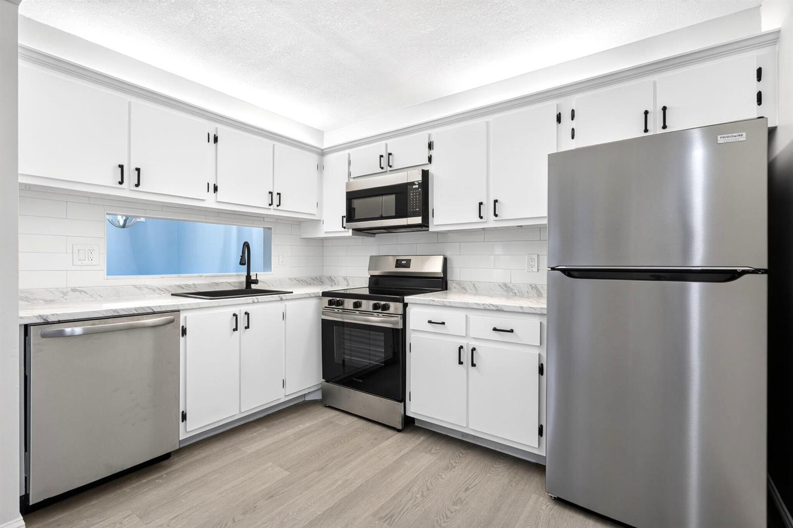 A kitchen with white cabinets, stainless steel appliances, marble-look countertops, and light wood flooring — 6495 Chasewood Drive # B, Jupiter FL 33458, JUPITER, FL