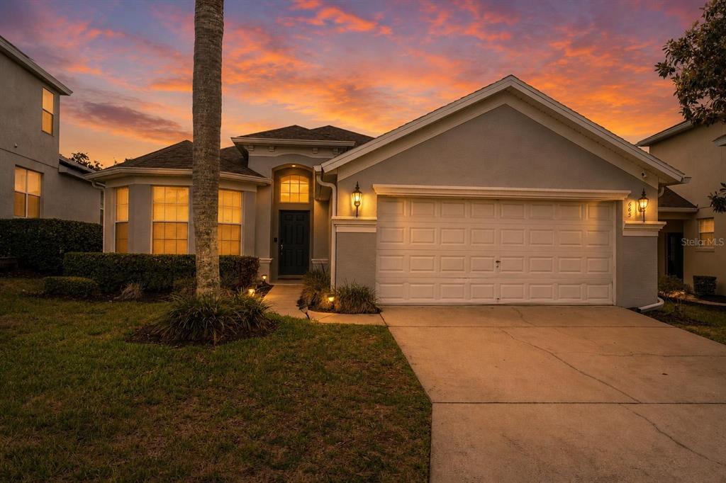 A single-story suburban house with a two-car garage and a sunset sky background — 665 MONTARA DRIVE, DAVENPORT, FL