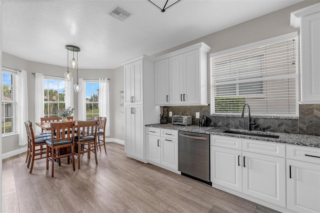 A kitchen with white cabinets, granite countertops, a stainless steel dishwasher, and an adjacent dining area — 665 MONTARA DRIVE, DAVENPORT, FL