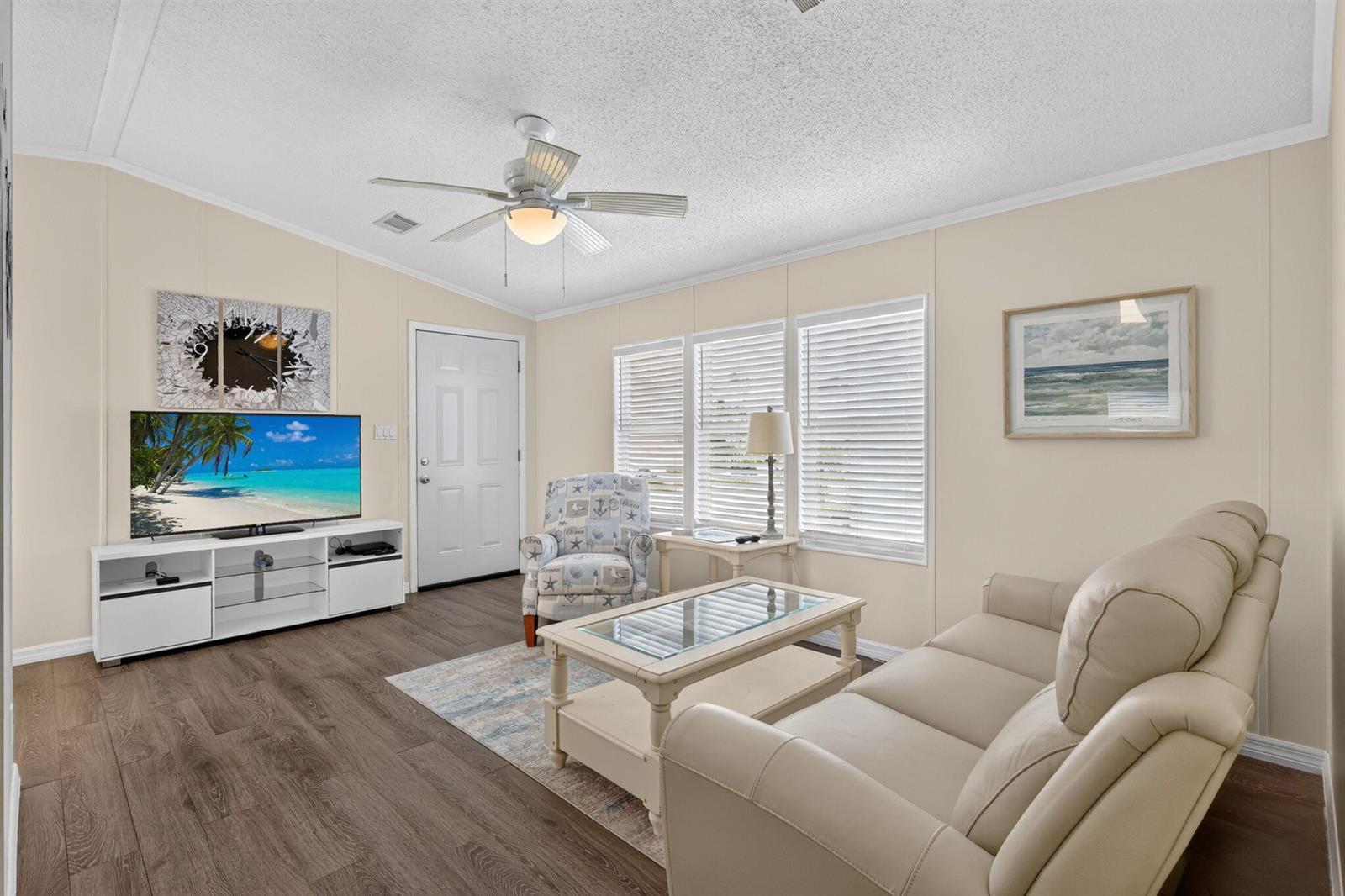 A living room features a beige sofa, a patterned armchair, a glass-topped coffee table, and flooring — 351 Nettles Boulevard, Jensen Beach FL 34957, JENSEN BEACH, FL