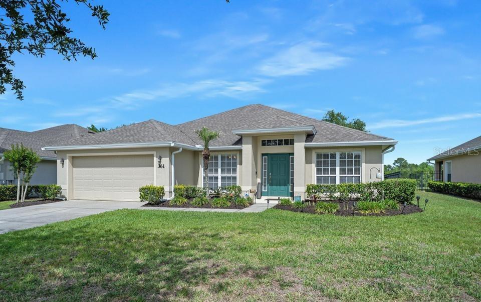 A single-story suburban house with a tan stucco exterior, a two-car garage, and a green door — 361 PERFECT DRIVE, DAYTONA BEACH, FL