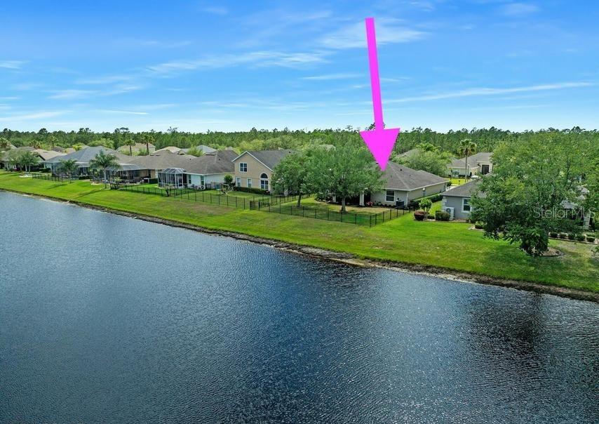 An aerial view shows a suburban house with a fenced backyard overlooking a large lake — 361 PERFECT DRIVE, DAYTONA BEACH, FL