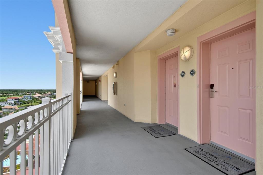 An outdoor hallway features two pink doors, gray flooring, and a white metal railing — 200 OCEAN CREST DRIVE UNIT 924, PALM COAST, FL