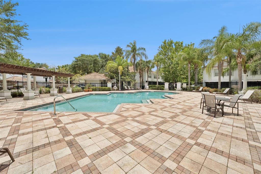 A swimming pool with a paved deck and a pergola sits outside a residential building — 7138 SHOWCASE LN, ORLANDO, FL