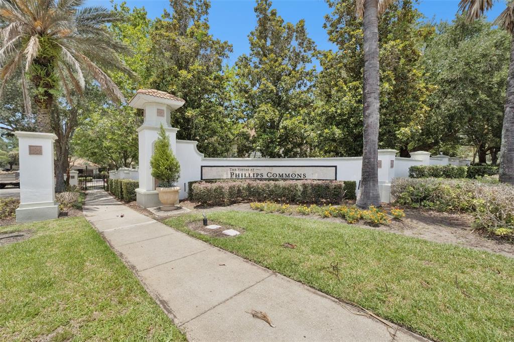 A concrete sidewalk leads to the white stucco entrance sign for The Vistas at Phillips Commons — 7138 SHOWCASE LN, ORLANDO, FL