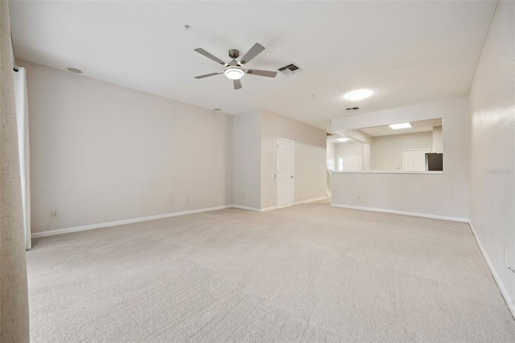 A spacious, carpeted living room features a ceiling fan and an open pass-through to the kitchen — 7138 SHOWCASE LN, ORLANDO, FL