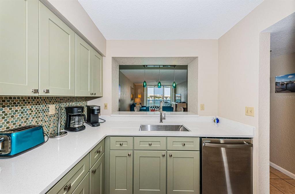 A kitchen features sage green cabinets, white countertops, a mosaic backsplash, and a pass-through window — 5901 BAHIA DEL MAR CIRCLE UNIT 518, ST PETERSBURG, FL