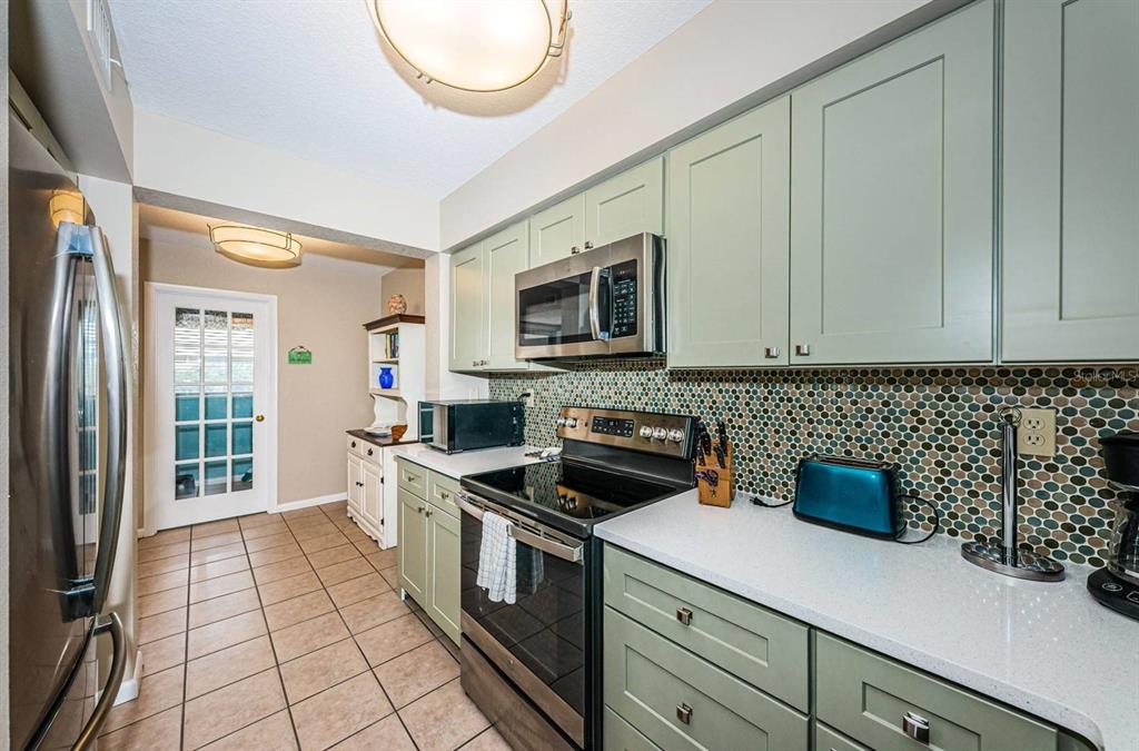 A kitchen features sage green cabinets, a mosaic tile backsplash, and stainless steel appliances — 5901 BAHIA DEL MAR CIRCLE UNIT 518, ST PETERSBURG, FL