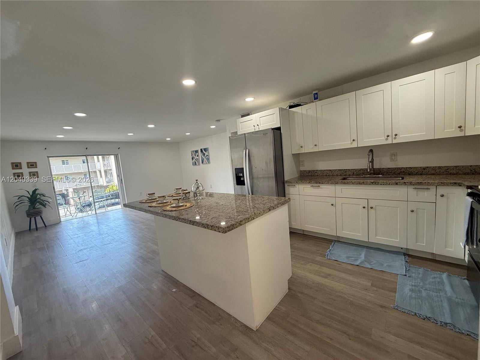 A kitchen features white cabinets, granite countertops, a center island, and light wood-look flooring — 6780 W 2nd Ct # 212, Hialeah FL 33012, HIALEAH, FL