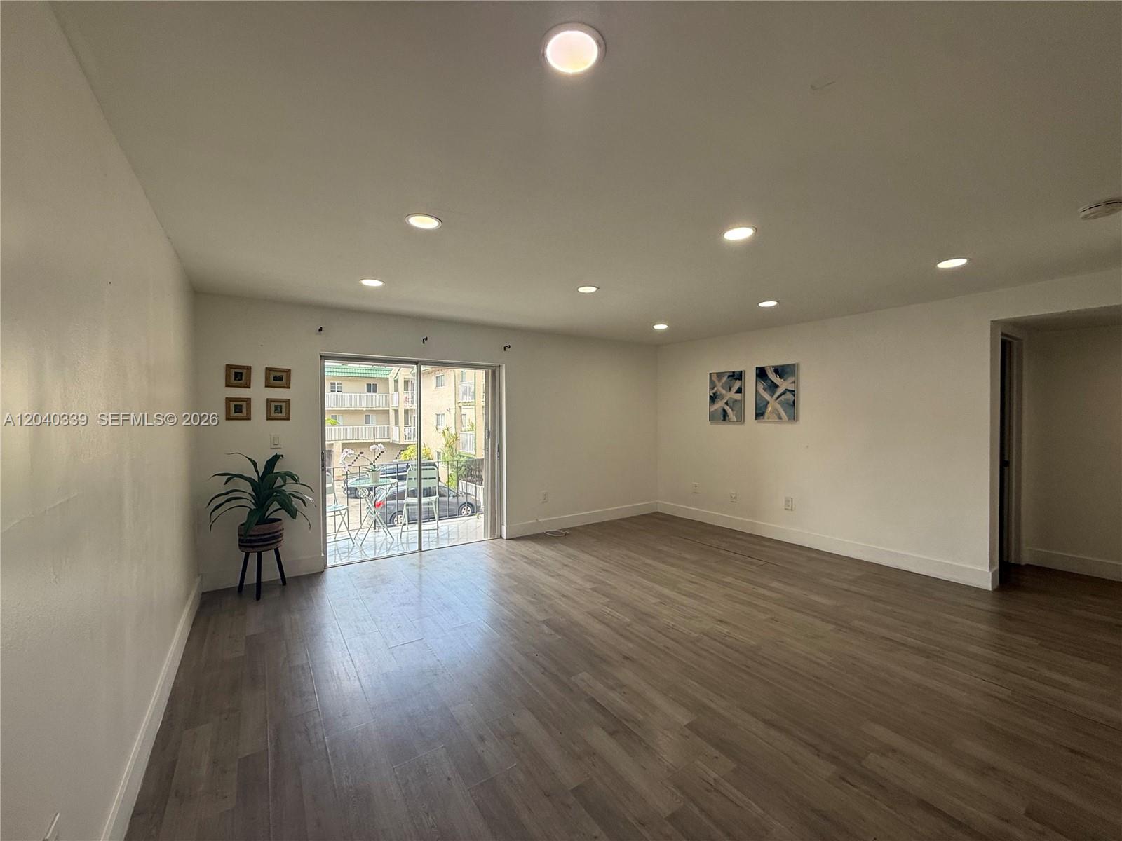An empty living room features wood-look flooring, recessed lighting, and a sliding glass balcony door — 6780 W 2nd Ct # 212, Hialeah FL 33012, HIALEAH, FL