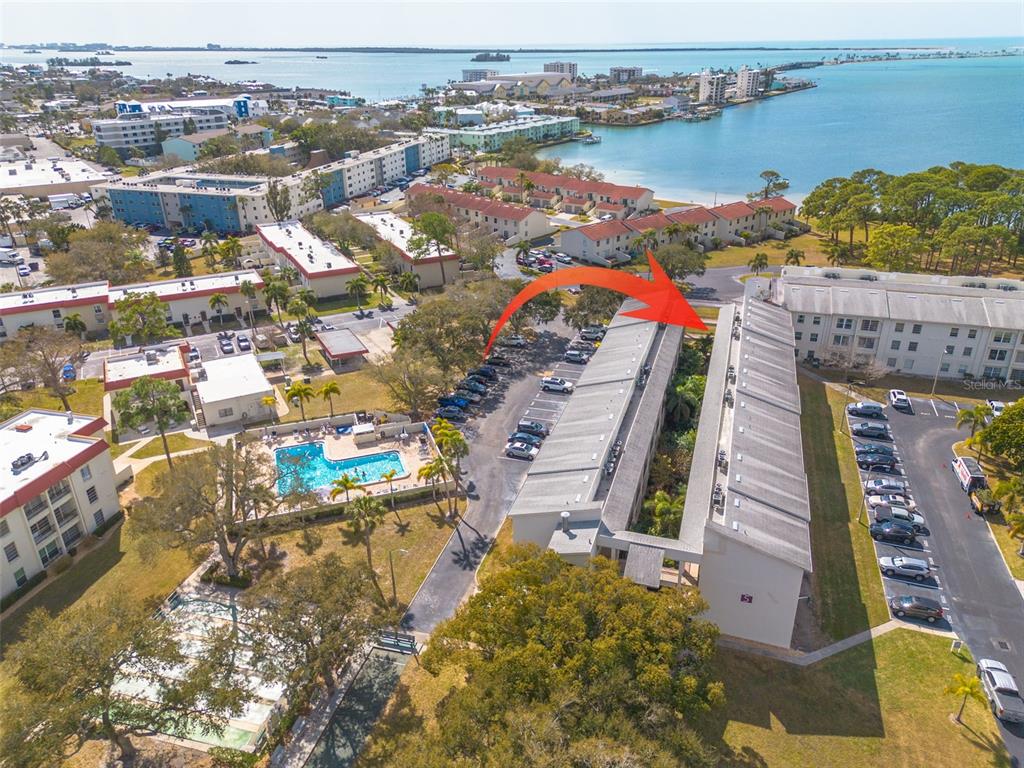 An aerial view shows a multi-story apartment complex with a swimming pool and parking lots — 2700 BAYSHORE BOULEVARD UNIT 5302, DUNEDIN, FL