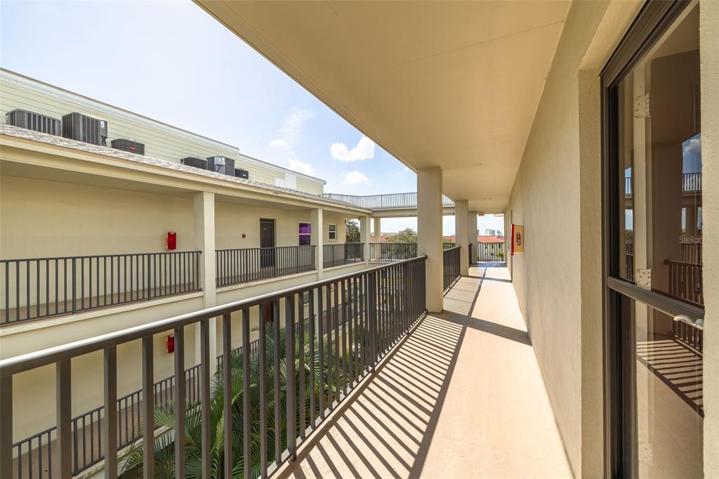 An outdoor covered walkway with metal railings overlooks a courtyard with palm trees — 2700 BAYSHORE BOULEVARD UNIT 5302, DUNEDIN, FL