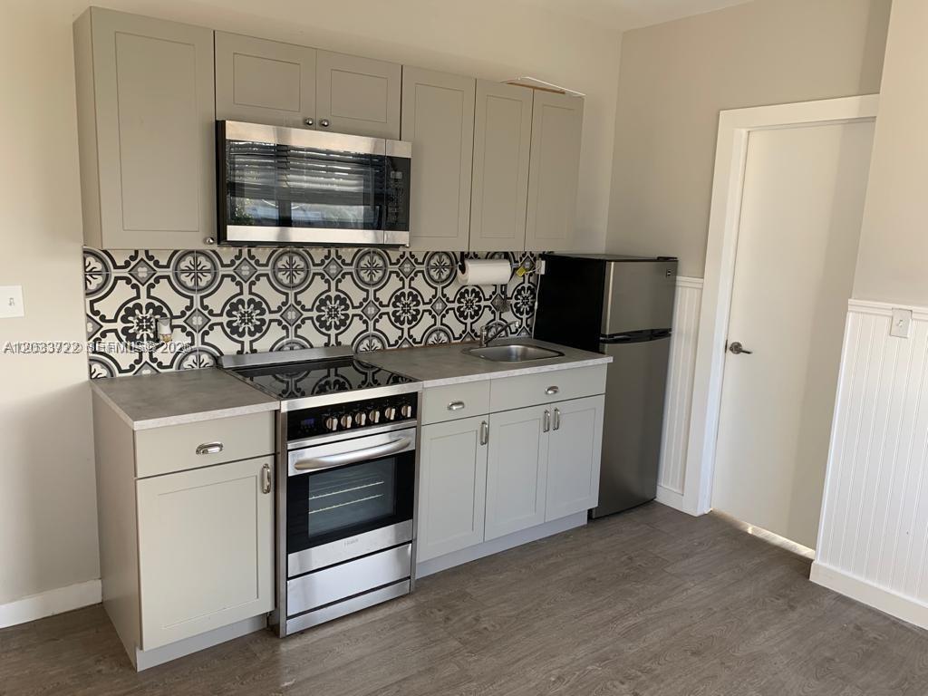 A small kitchen features gray cabinets, a patterned tile backsplash, and stainless steel appliances — 2932 NW 16th Ave # 3A, Miami FL 33142, MIAMI, FL