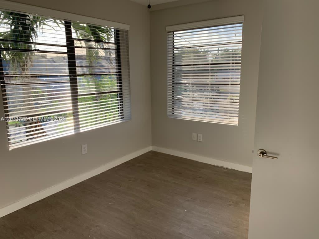 An empty room features light gray walls, wood-look flooring, and two windows with horizontal blinds — 2932 NW 16th Ave # 3A, Miami FL 33142, MIAMI, FL