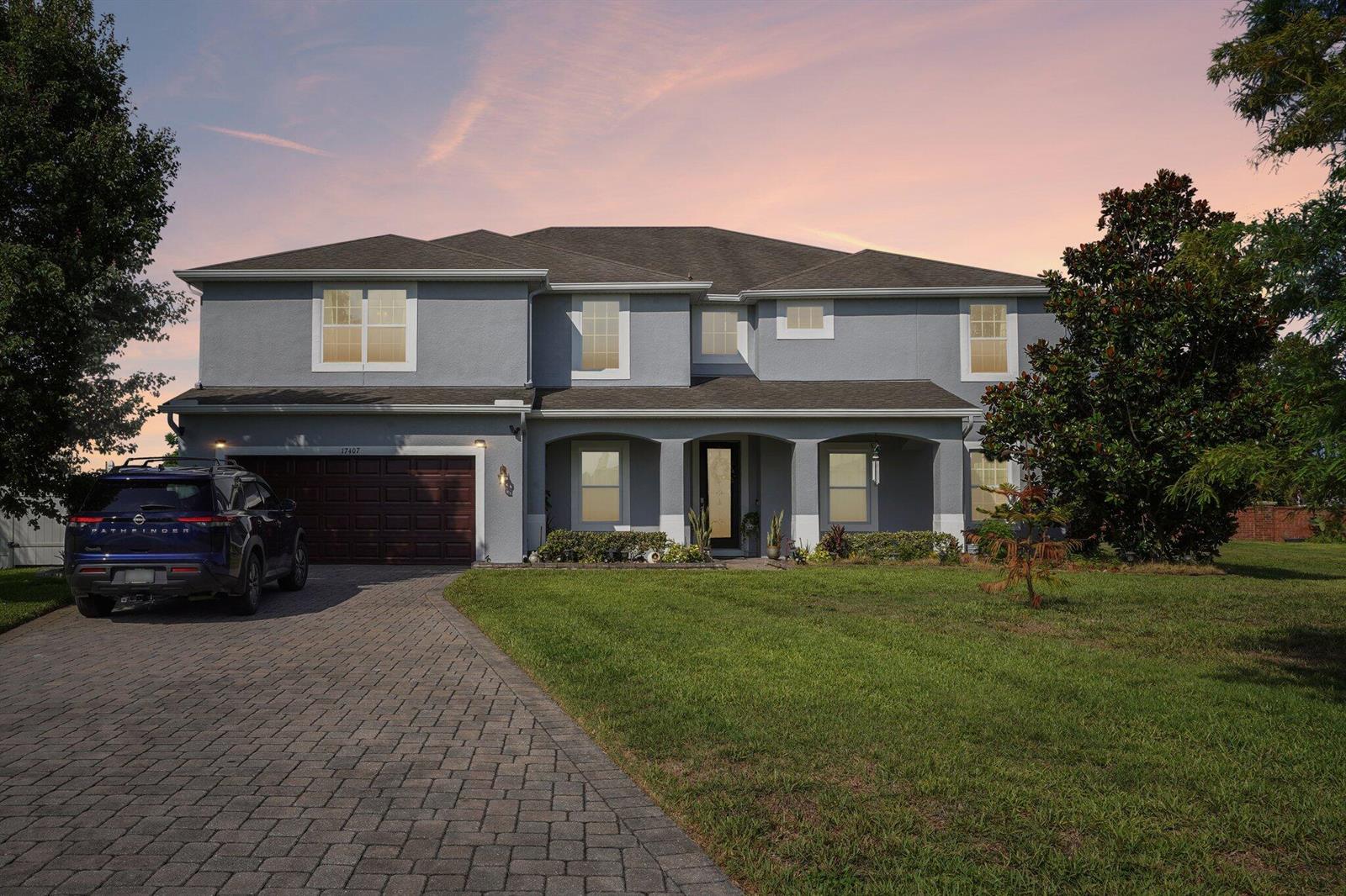 A two-story gray house with a paved driveway, a dark garage door, and a front porch — 17407 Bella Nova Drive, Orlando FL 32820, ORLANDO, FL
