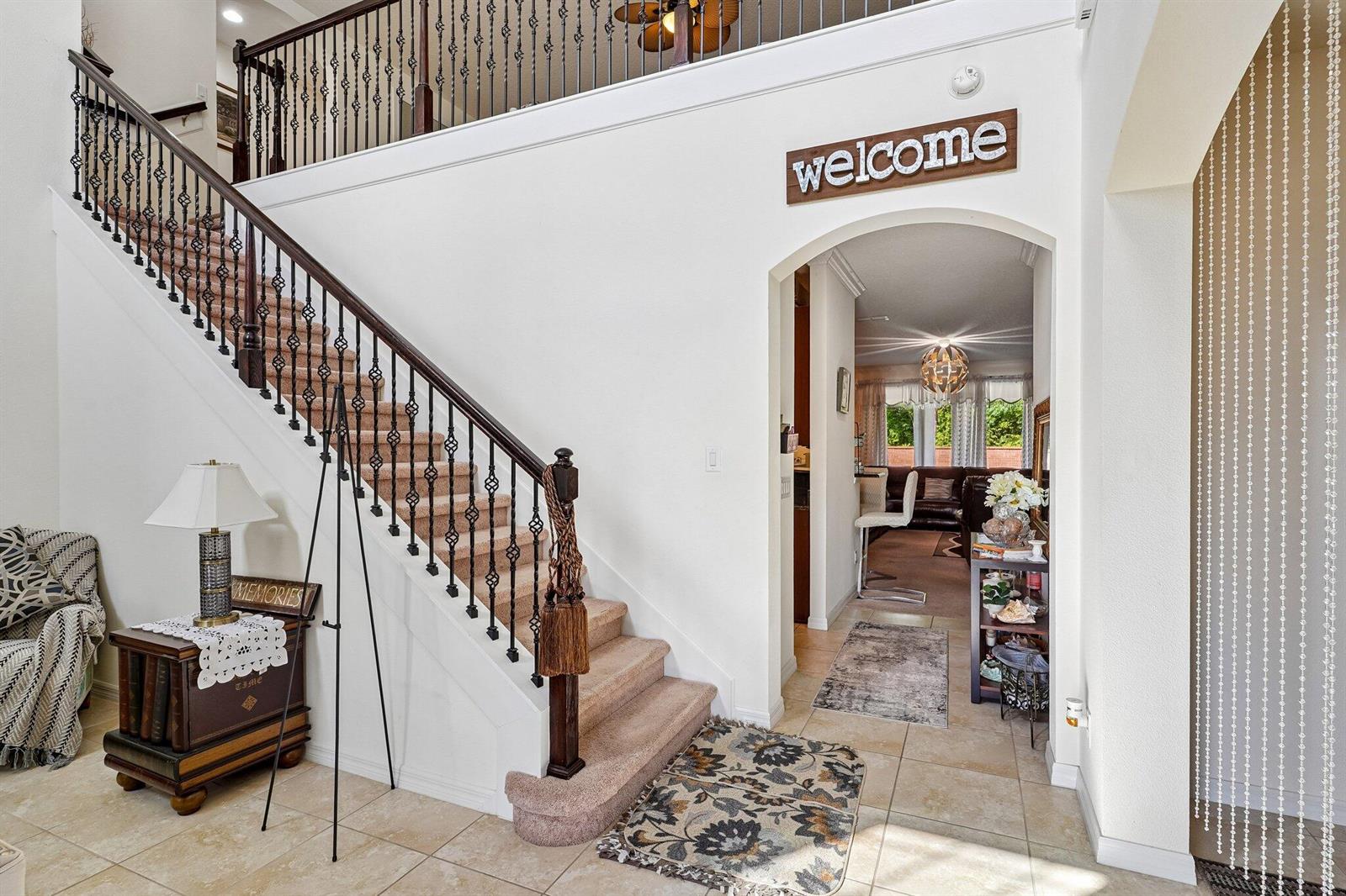 A foyer features a carpeted staircase with iron railings, tile flooring, and a welcome sign — 17407 Bella Nova Drive, Orlando FL 32820, ORLANDO, FL