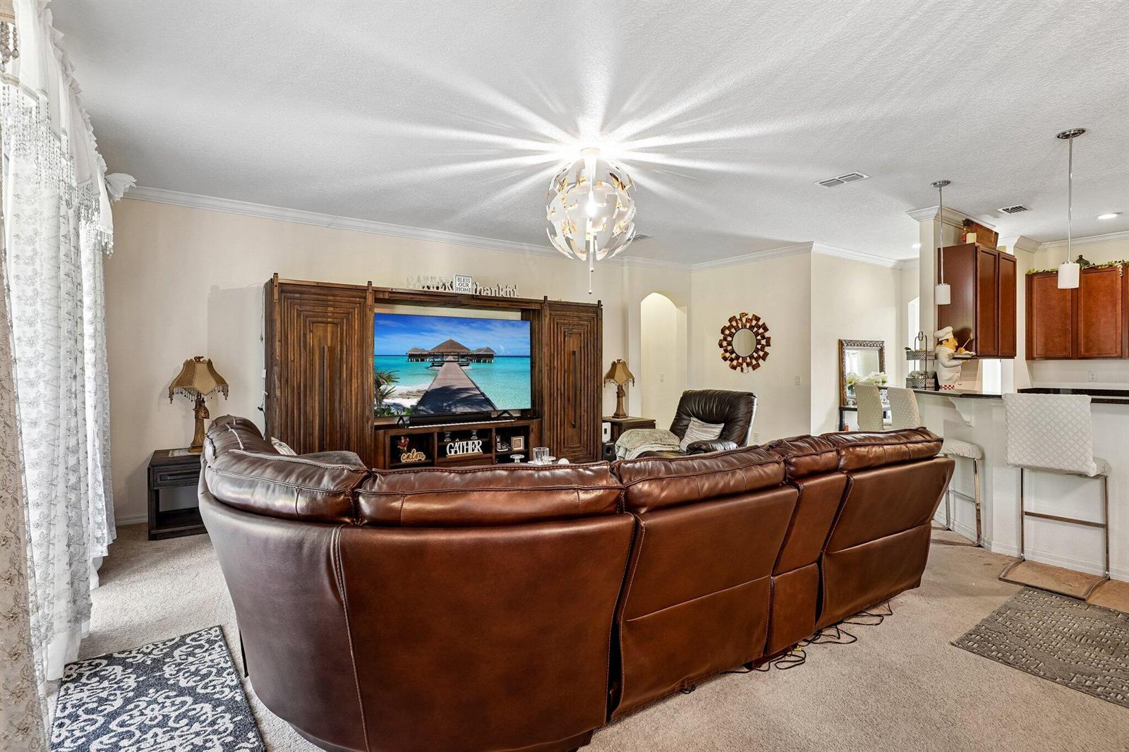 A living room features a large brown leather sectional, an entertainment center, and kitchen bar seating — 17407 Bella Nova Drive, Orlando FL 32820, ORLANDO, FL
