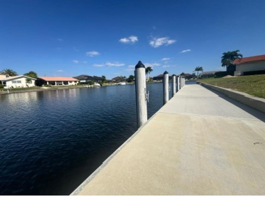 A concrete boat dock extends along a canal lined with houses under a clear sky — 402 VALLETTA COURT, PUNTA GORDA, FL