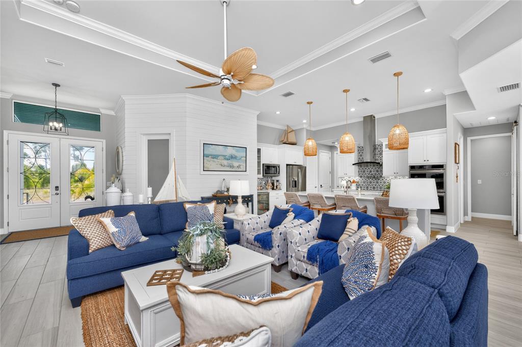 A bright open-concept living room and kitchen featuring blue sofas, patterned armchairs, and coastal decor — 255 ROTONDA BOULEVARD S, ROTONDA WEST, FL