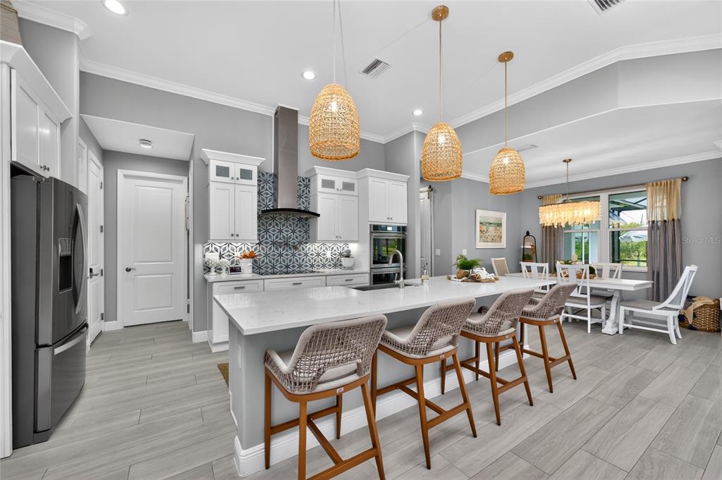 A modern kitchen features white cabinetry, a patterned backsplash, a large island, and woven pendant lights — 255 ROTONDA BOULEVARD S, ROTONDA WEST, FL