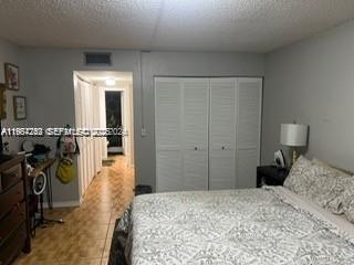 A bedroom features a bed with patterned bedding, white louvered closet doors, and tile flooring — 3253 Foxcroft Rd # G107, Miramar FL 33025, MIRAMAR, FL