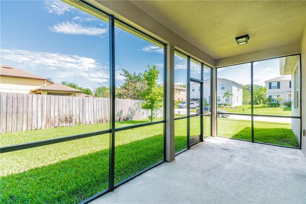 A screened-in concrete patio overlooks a grassy backyard with a wooden fence and neighboring houses — 1501 ANGLER AVENUE, KISSIMMEE, FL