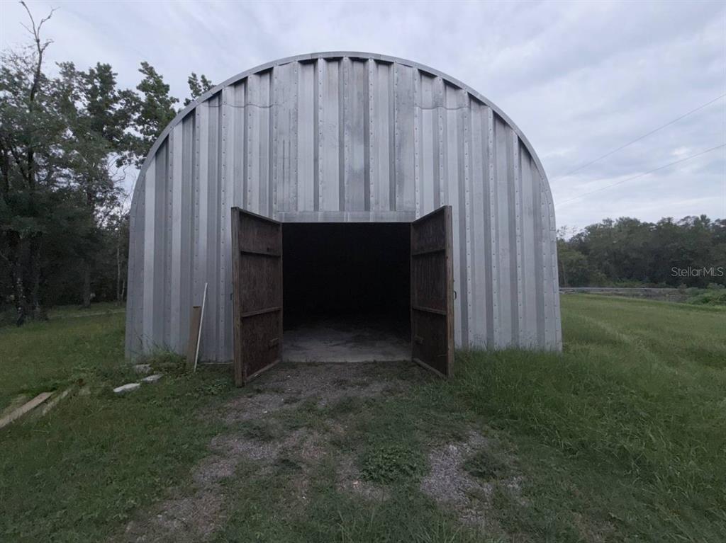 A metal Quonset-style storage building with open double doors stands in a grassy field — 10600 W DEEP CREEK BOULEVARD, HASTINGS, FL