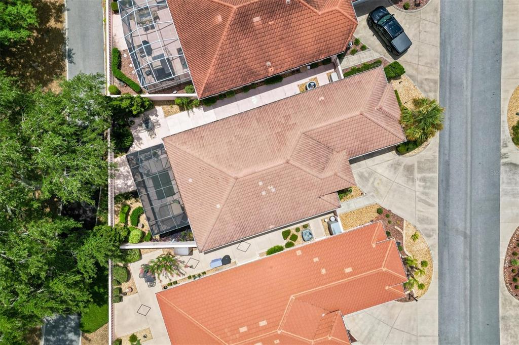 An aerial view shows three houses with tiled roofs, screened-in lanais, and paved driveways — 1516 MARTINEZ DRIVE, LADY LAKE, FL