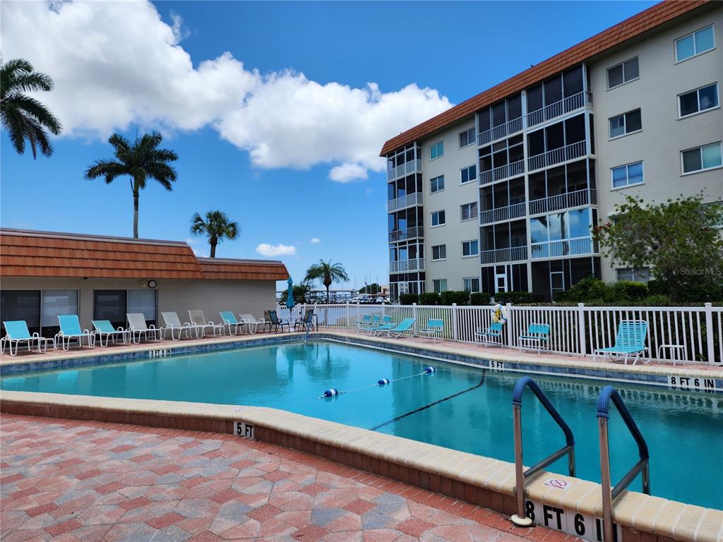 A swimming pool with a white fence sits in front of a multi-story apartment building — 1650 1ST AVENUE W UNIT 408B, BRADENTON, FL