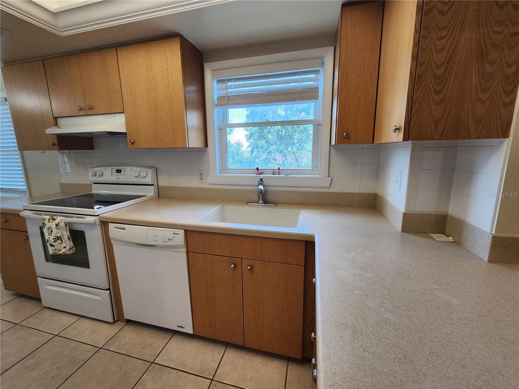 A kitchen features wood cabinets, white appliances, a white sink, and light-colored countertops — 1650 1ST AVENUE W UNIT 408B, BRADENTON, FL