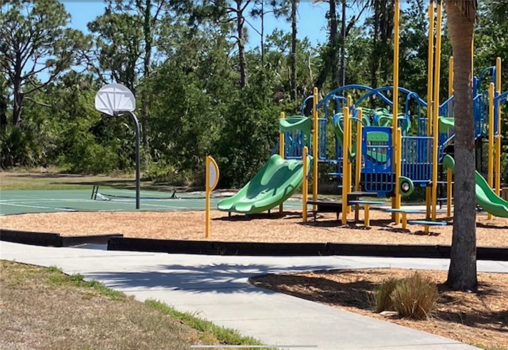 A playground with a green slide and a basketball hoop next to a paved path — 13232 KITCHENER AVENUE, PORT CHARLOTTE, FL