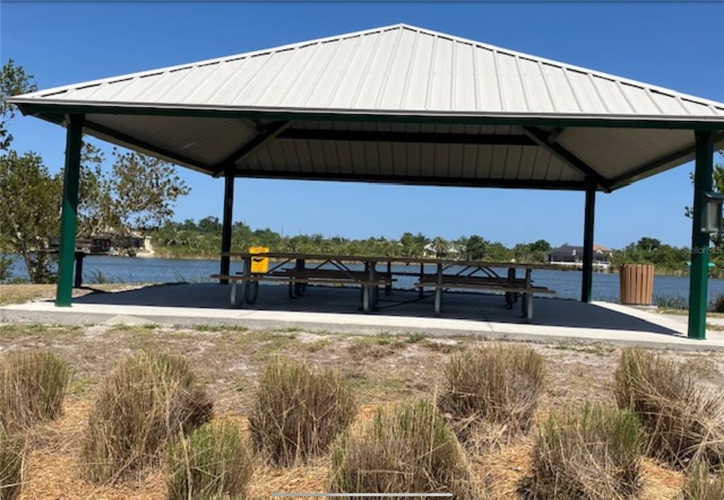 A metal-roofed pavilion with picnic tables sits on a concrete pad overlooking a lake — 13232 KITCHENER AVENUE, PORT CHARLOTTE, FL