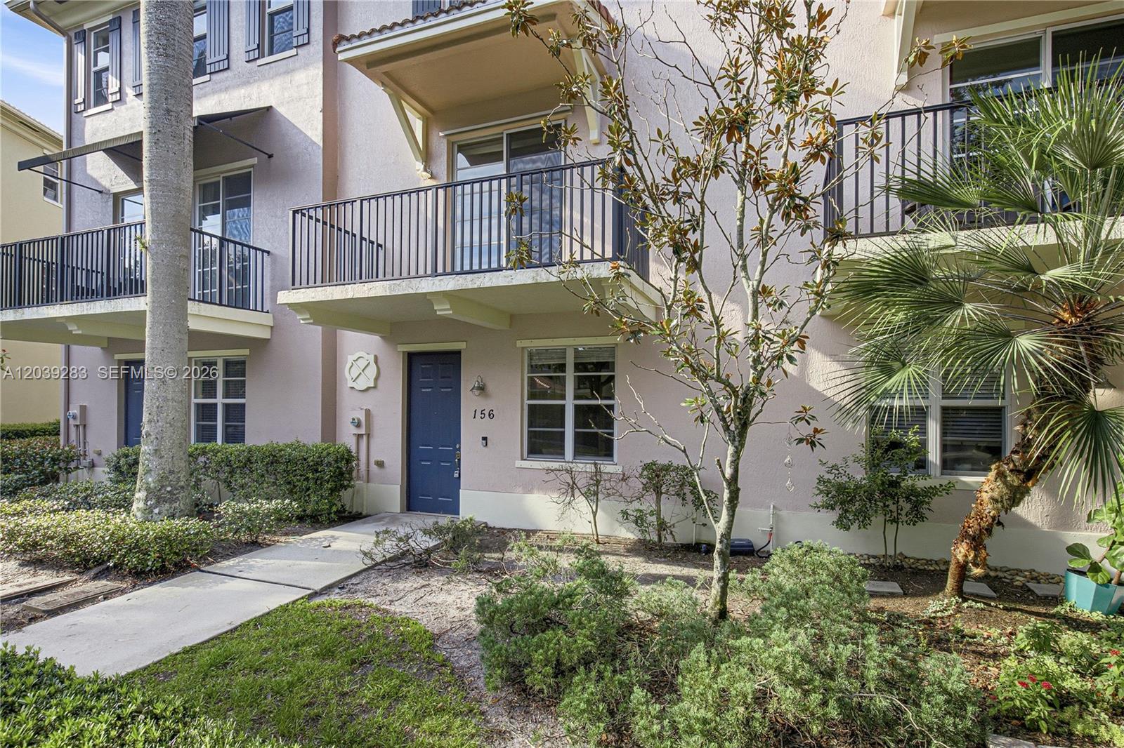 The exterior of a two-story townhouse features a blue front door, balcony, and landscaping — 156 Greenwich Cir, Jupiter FL 33458, JUPITER, FL