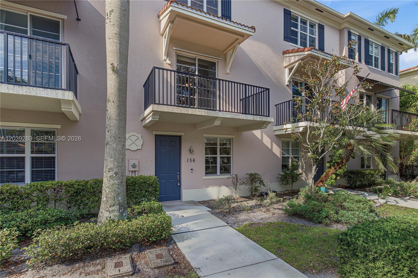 A multi-story townhouse exterior features a blue front door, balconies, and a concrete walkway — 156 Greenwich Cir, Jupiter FL 33458, JUPITER, FL