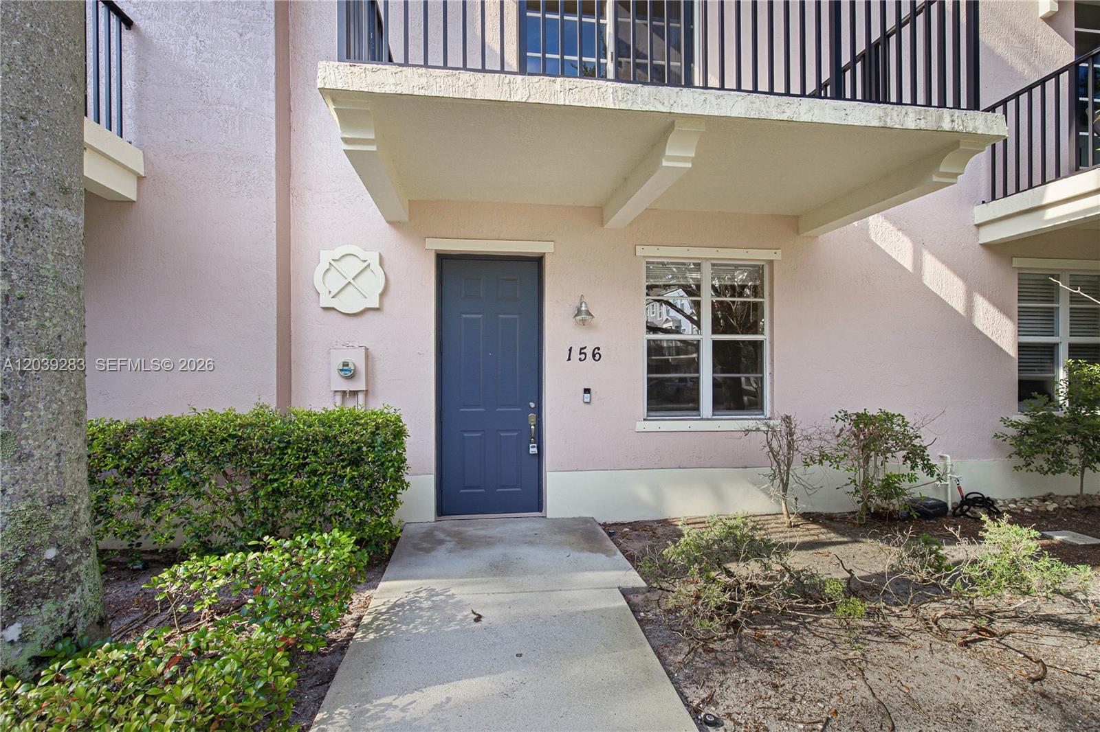 The exterior of a pink building features a blue front door labeled 156 — 156 Greenwich Cir, Jupiter FL 33458, JUPITER, FL