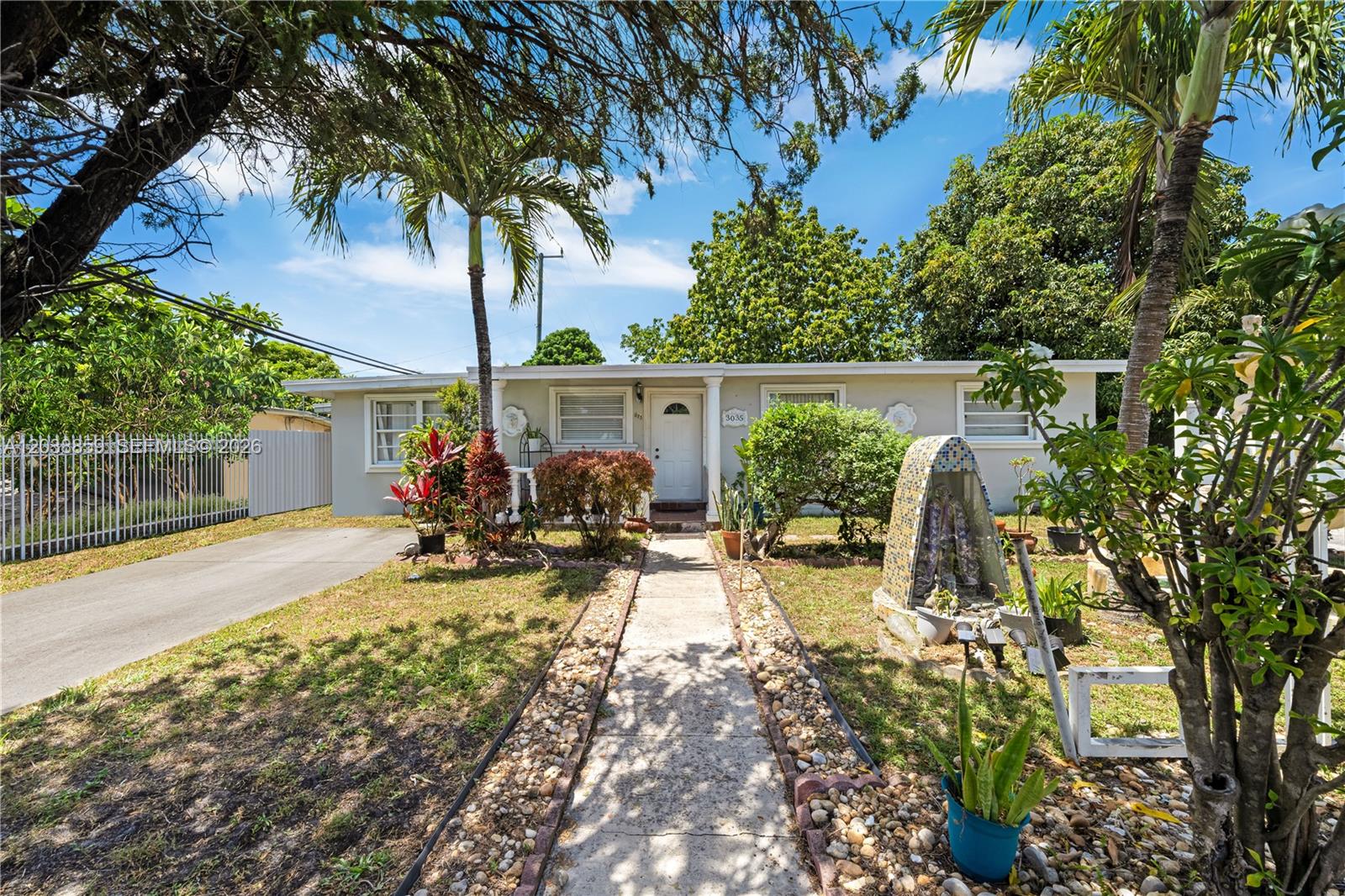 A single-story house with a concrete walkway, palm trees, and a tiled garden shrine — 3035 NW 83rd St, Miami FL 33147, MIAMI, FL