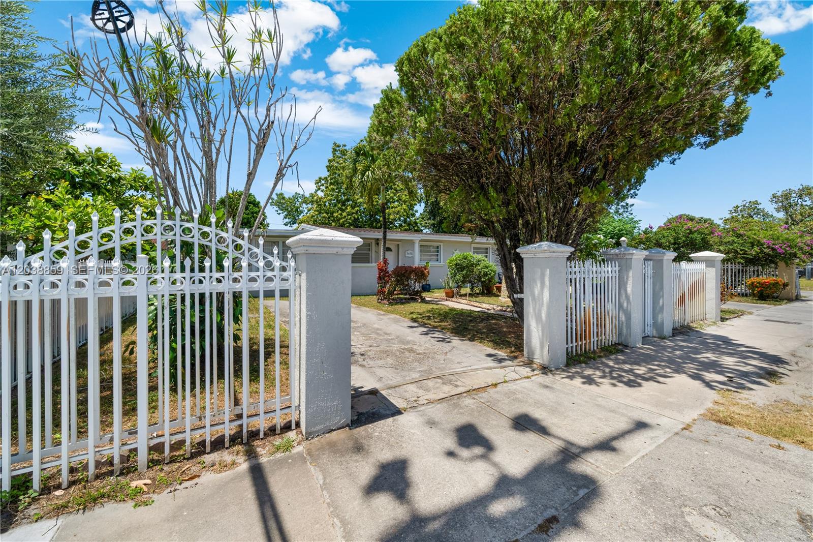 A white metal fence with concrete pillars stands in front of a single-story house — 3035 NW 83rd St, Miami FL 33147, MIAMI, FL