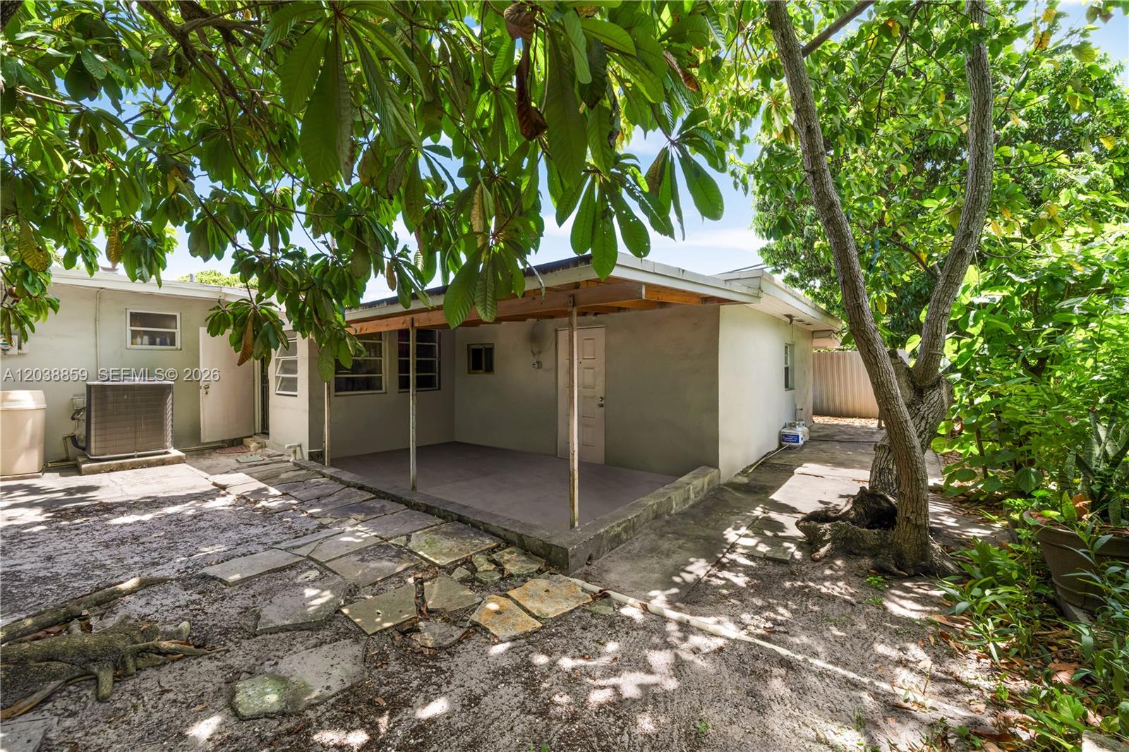 A concrete patio with a covered roof sits beside a house with a tree — 3035 NW 83rd St, Miami FL 33147, MIAMI, FL