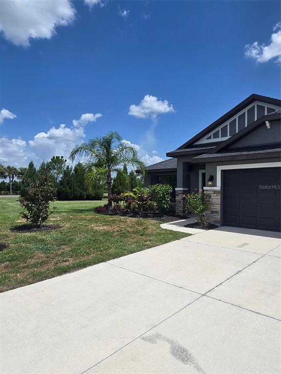A single-story house with a dark garage door, stone accents, and a landscaped front yard — 16215 59TH COURT E, PARRISH, FL