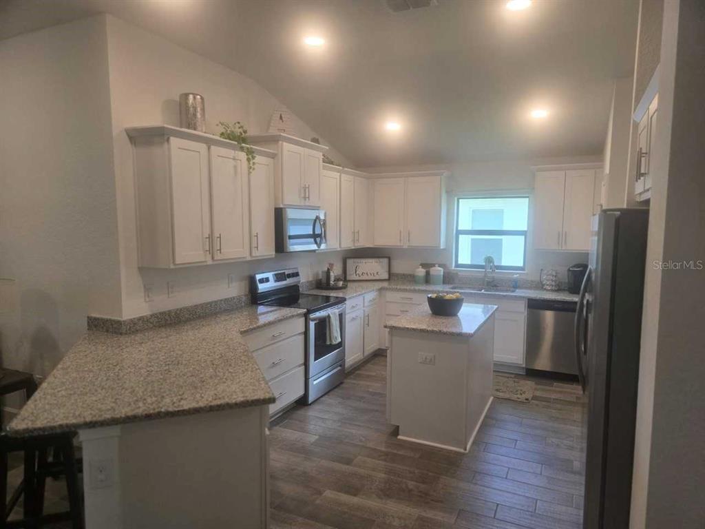 A kitchen features white cabinets, granite countertops, a center island, and wood-look tile flooring — 16215 59TH COURT E, PARRISH, FL