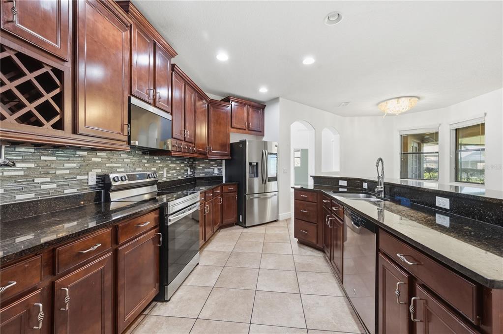 A kitchen features dark wood cabinets, granite countertops, stainless steel appliances, and a tiled backsplash — 3950 SUNSET LAKE DRIVE, LAKELAND, FL