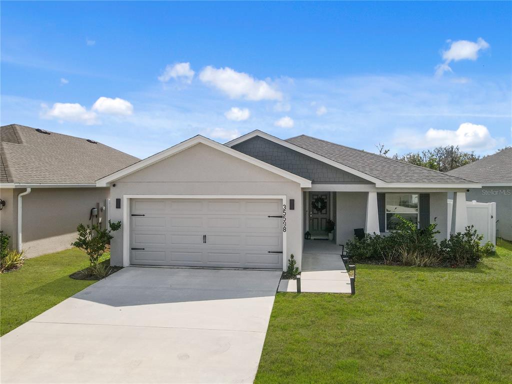 A single-story house features a two-car garage, a covered entryway, and a gray shingled roof — 35598 BELLINGTON BOULEVARD, ZEPHYRHILLS, FL