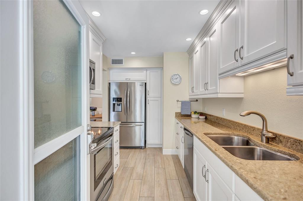 A galley kitchen features white cabinets, stainless steel appliances, granite countertops, and wood-look tile flooring — 137 AVENIDA MESSINA UNIT 3, SARASOTA, FL